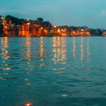 Illuminated riverfront in Varanasi with floating diyas at dusk.