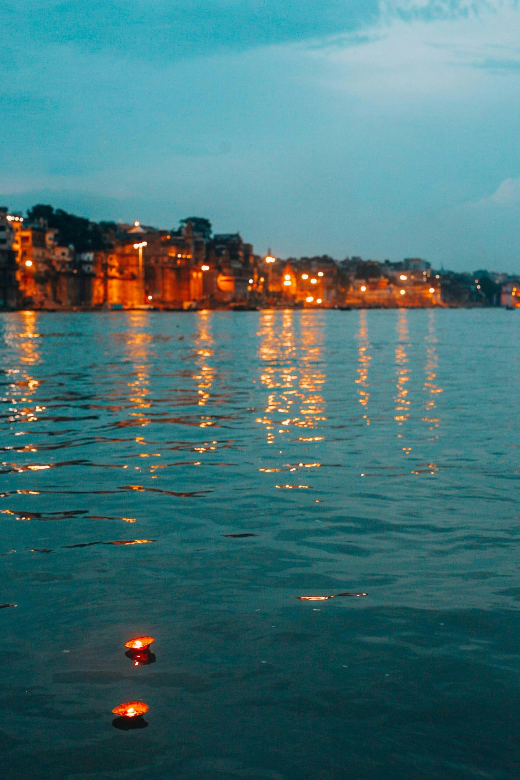 Illuminated riverfront in Varanasi with floating diyas at dusk.
